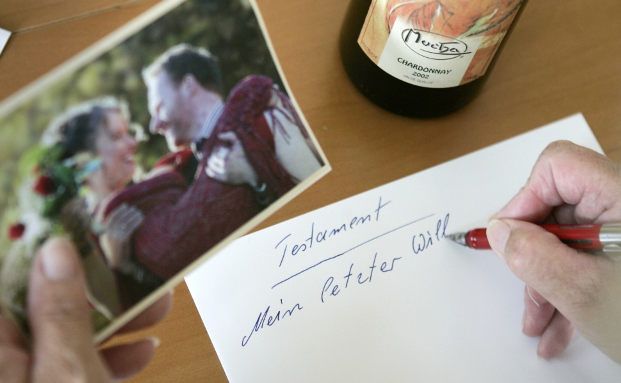 Eine Person verfasst handschriftlich auf einem Blatt Papier ein Testament.