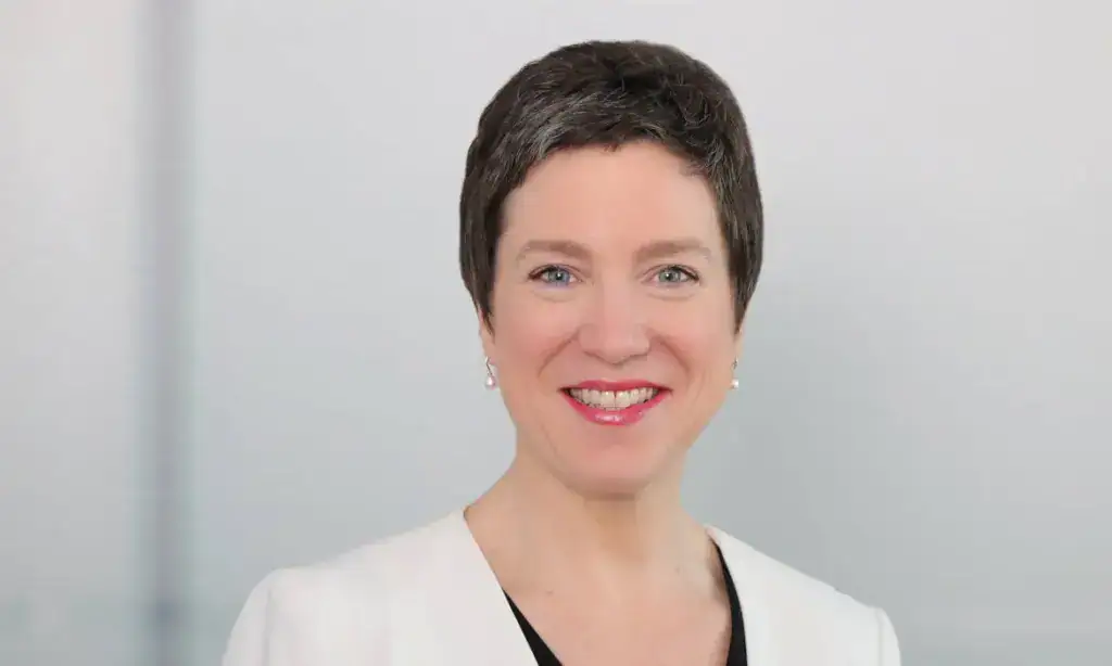 Professionelle Frau mit kurzen braunen Haaren, freundlich lächelnd, im weißen Business-Outfit.