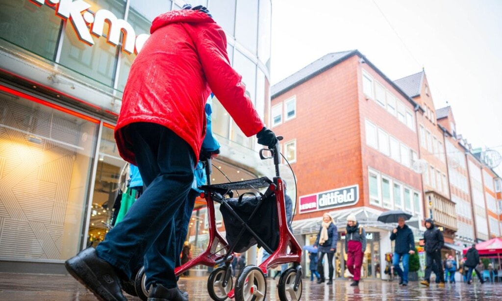 Senior mit Rollator vor Einkaufszentrum in der Stadt.