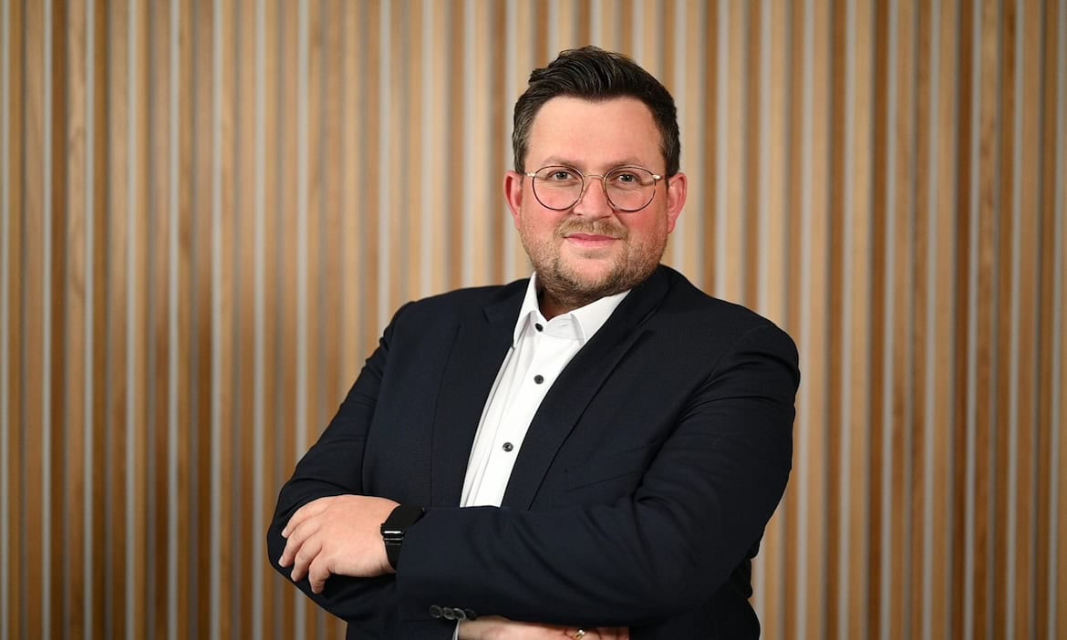 Portrait eines Mannes in Businesskleidung vor Holzpaneelwand.