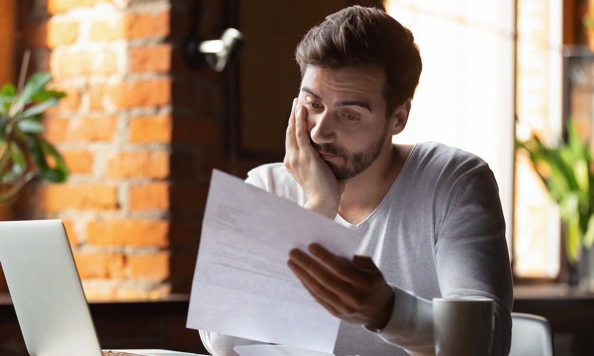 Nachdenklicher Mann liest Finanzdokumente, Sorgen wegen Altersvorsorge.