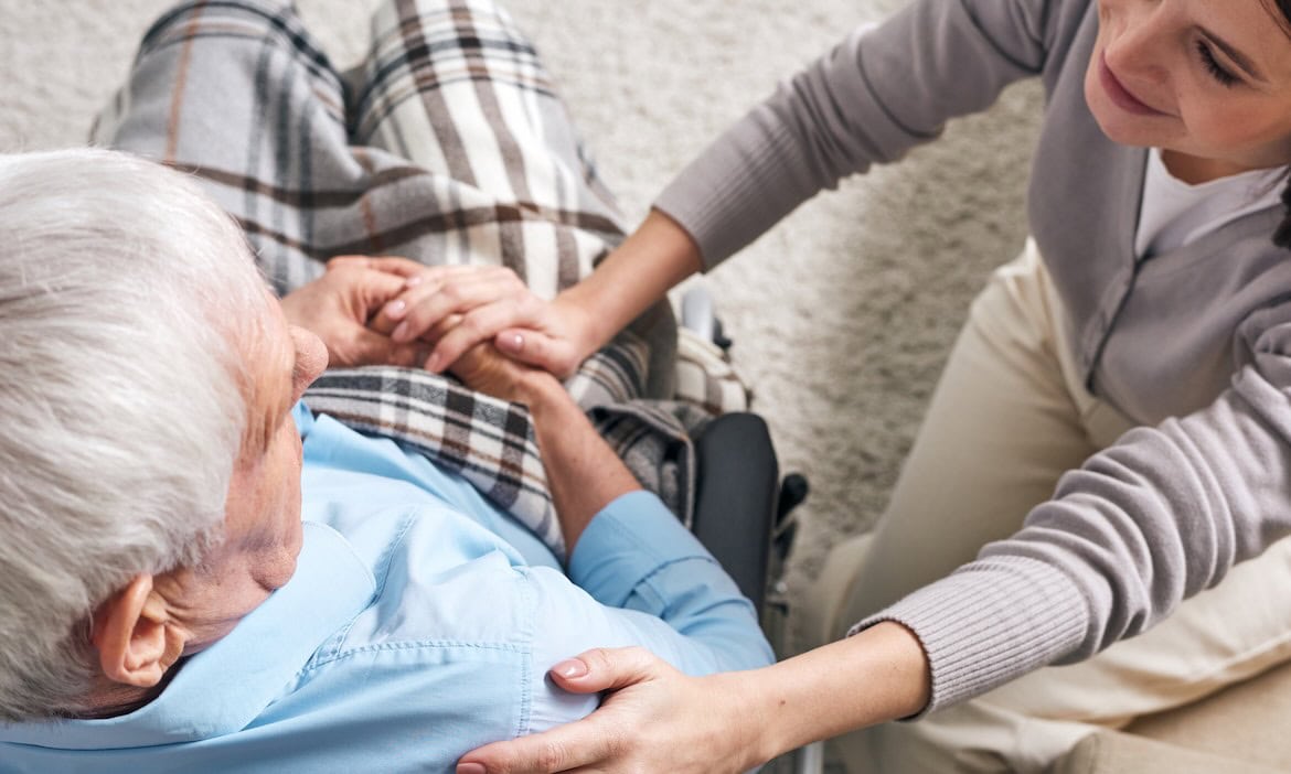 Frau unterstützt älteren Mann bei Pflegebedarf, betriebliche Pflegeversicherung.