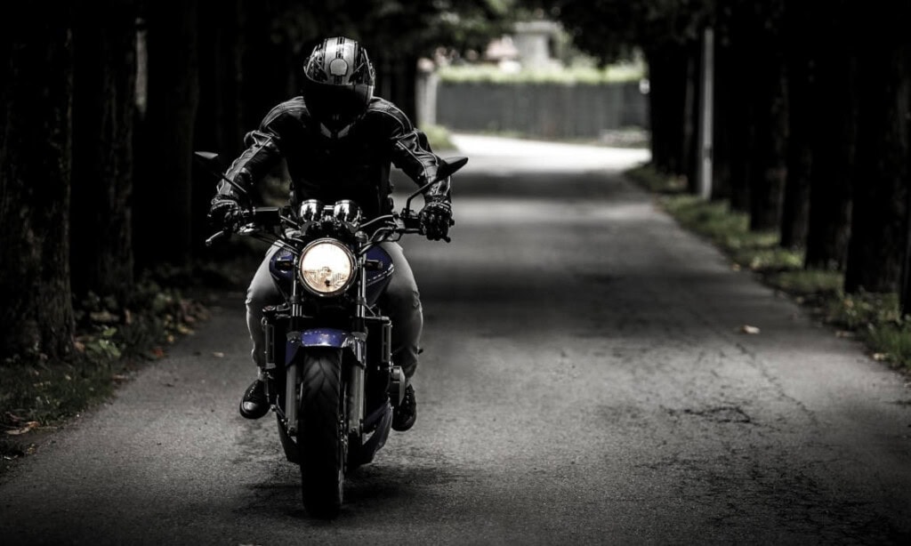 Motorradfahrer auf einer ruhigen, bewaldeten Straße, symbolisiert faire Versicherungsanbieter.