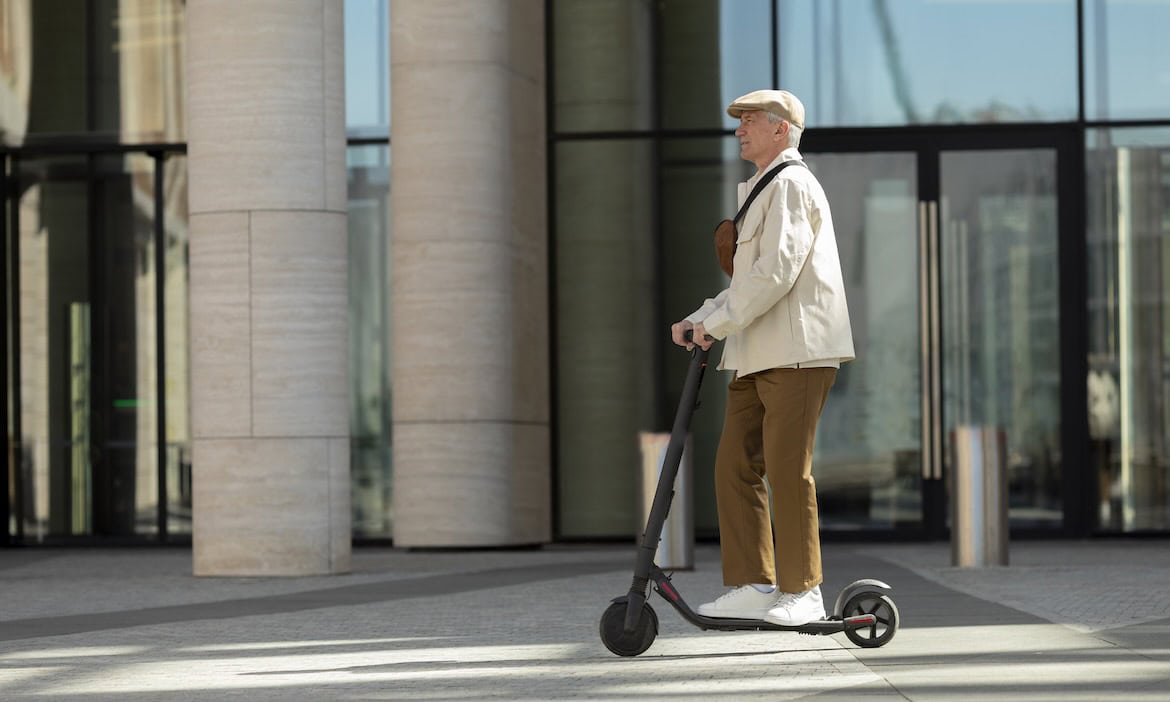 Älterer Mensch auf Elektroroller vor moderner Bürogebäude-Fassade.