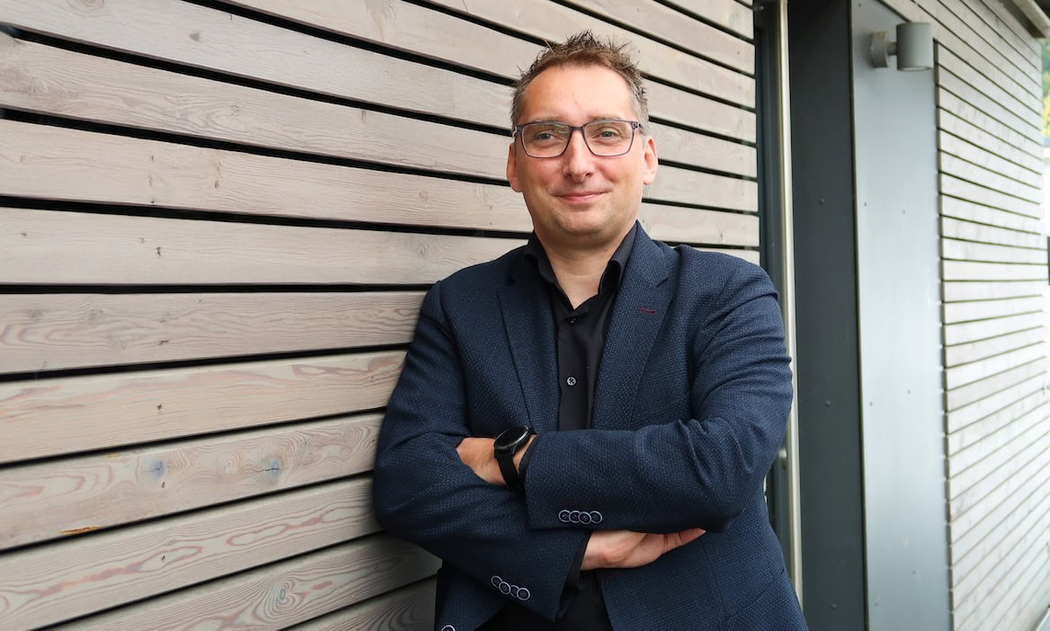 Geschäftsmann vor Holzfassade, nutzt KI für erfolgreiche Kundengespräche.