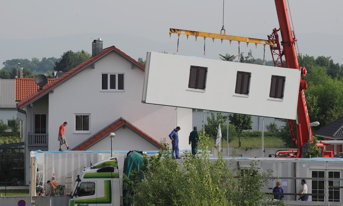 Kran hebt vorgefertigtes Hausmodul auf eine Baustelle.