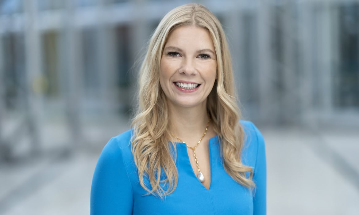 Frau mit blauer Bluse vor moderner Firmenfassade, symbolisiert Unternehmensfusion.