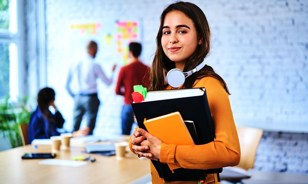 Junge Frau mit Büchern und Notizblock, bereit für den Unterricht, in einem hellen, modernen Klassenr.