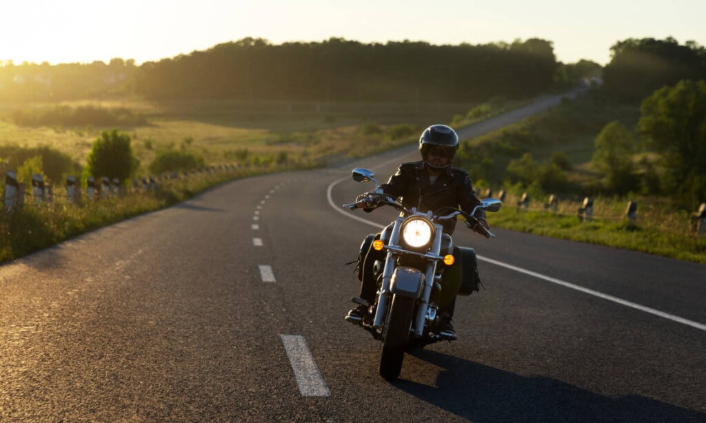 Motorradfahrer trägt Schutzhelm und -kleidung auf kurviger Landstraße bei Sonnenlicht.