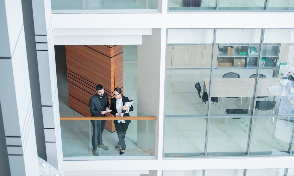 Zwei Makler im Gespräch in einem modernen Büro mit Glasfassade.