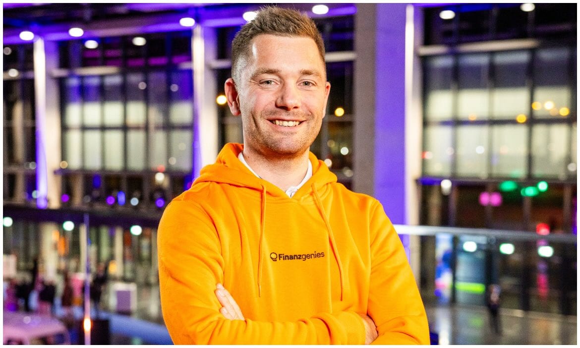 Mann in orange Hoodie vor moderner Firmenfassade, Experte für Altersvorsorge.