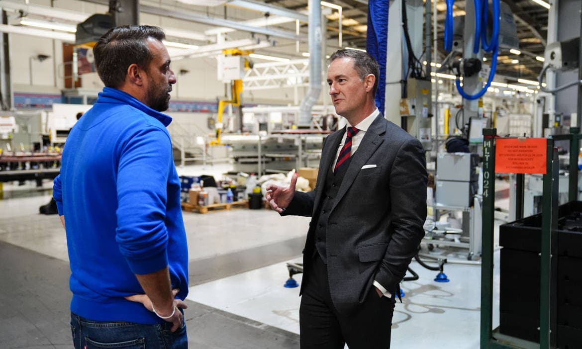 Zwei Männer im Gespräch in einer Fabrikhalle, diskutieren über Lieferketten und Versicherung.