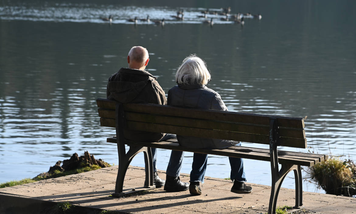 Älteres Paar sitzt entspannt am See und genießt die Natur.