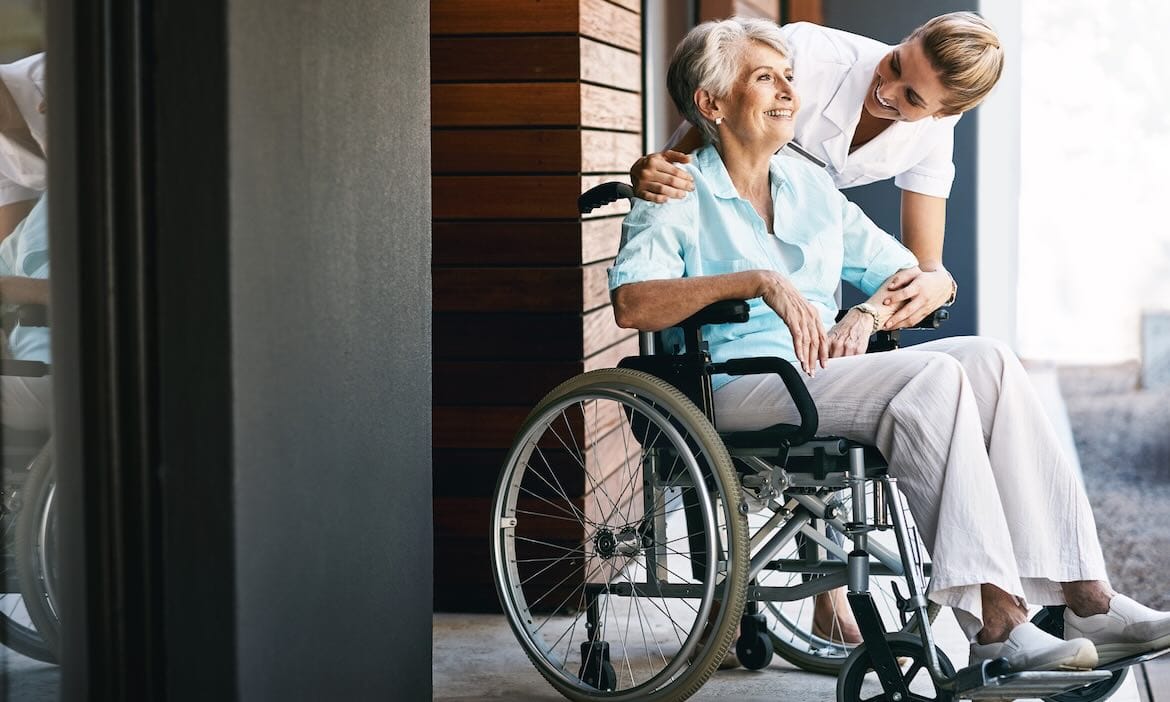 Ältere Frau im Rollstuhl erhält Pflegeberatung von Pflegekraft.