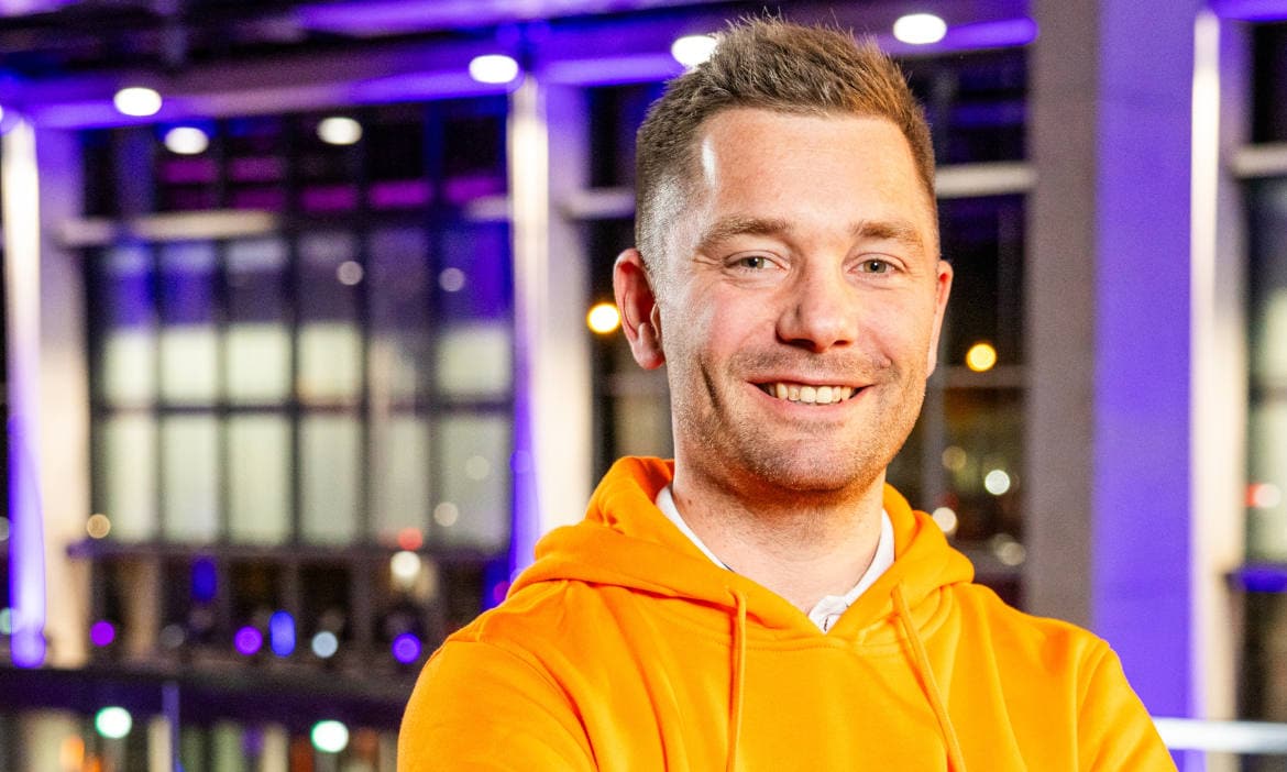 Mann in orange Hoodie vor moderner Bürofassade, Karrierewechsel zum Makler.