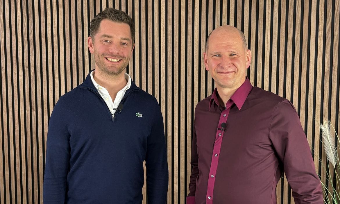 Zwei Männer in Businesskleidung vor modernem Holzdekor.