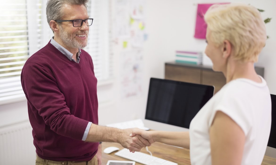 Mann und Frau schütteln sich die Hand in einem Büro, symbolisiert Kundenbindung bei Versicherern.