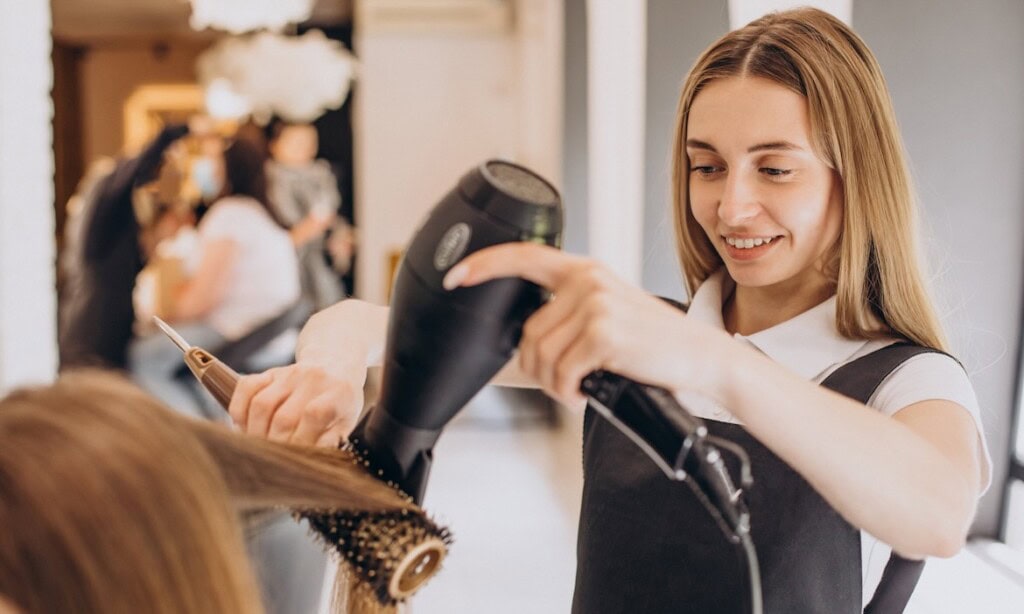 Friseurin trocknet Haare einer Kundin im Salon.