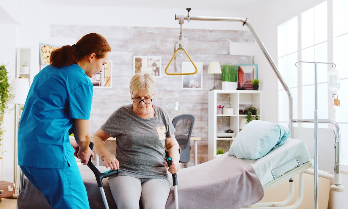 Pflegekraft unterstützt ältere Frau beim Aufstehen im Schlafzimmer.
