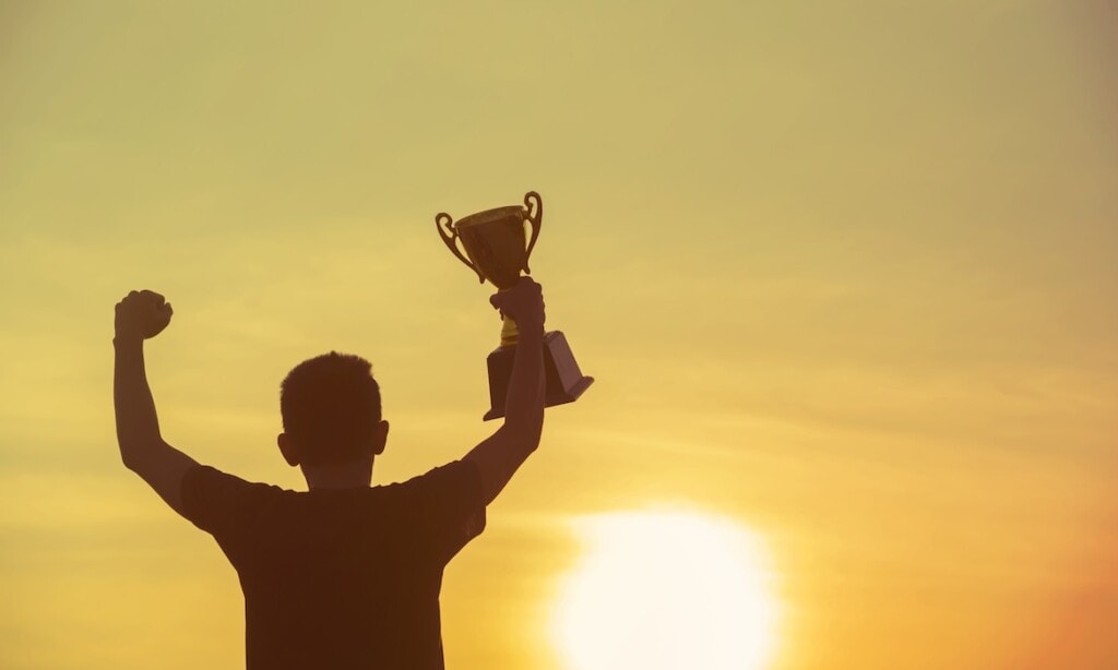 Mann hält Pokal hoch, symbolisiert Erfolg und Branchenbeste.