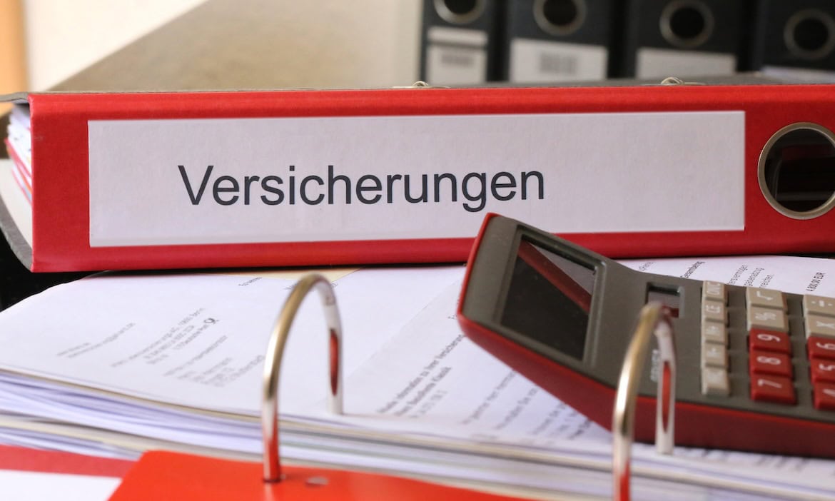 Büro mit Aktenordnern, Taschenrechner und Dokumenten zum Thema Versicherungen.