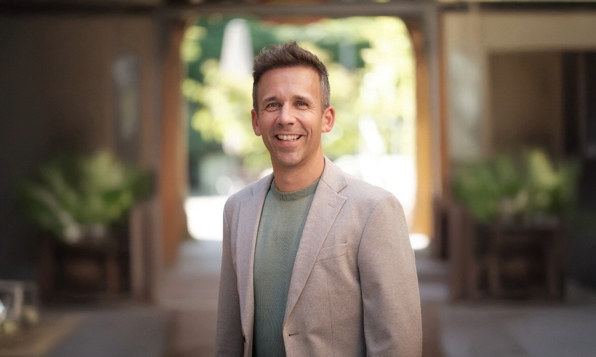 Lächelnder Makler vor modernem Büro mit CRM-Software im Hintergrund.