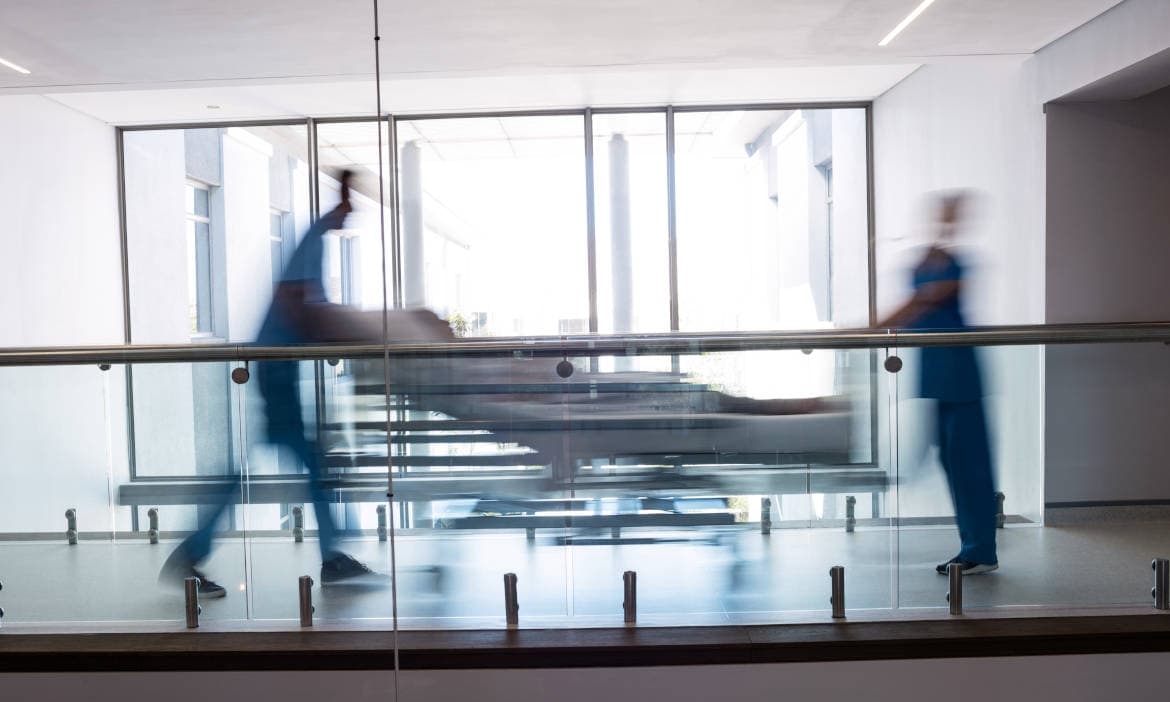 Pflegepersonal schiebt Krankenbett im Krankenhausflur, medizinischer Alltag.