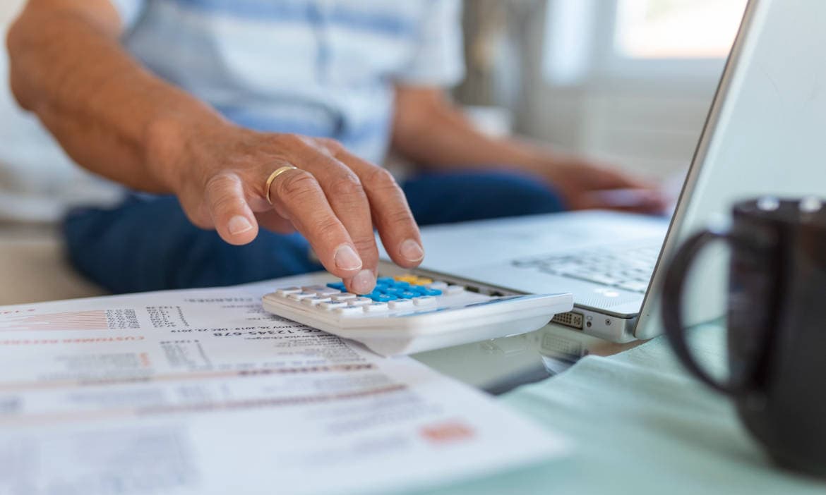 Person prüft Rechnungen am Laptop mit Taschenrechner.