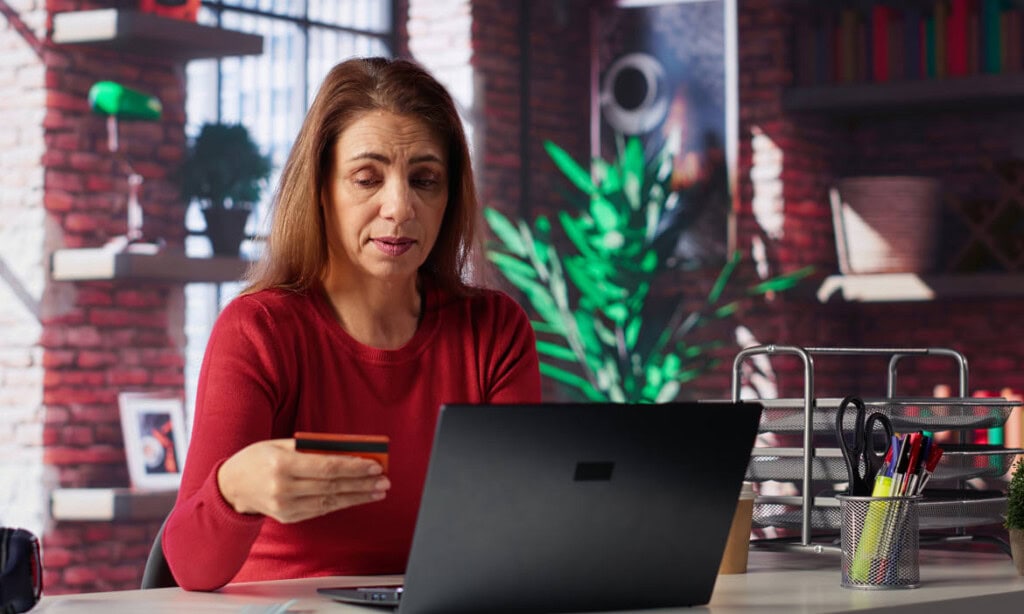 Frau prüft online Rentenauskunft am Laptop, hält Kreditkarte in der Hand.