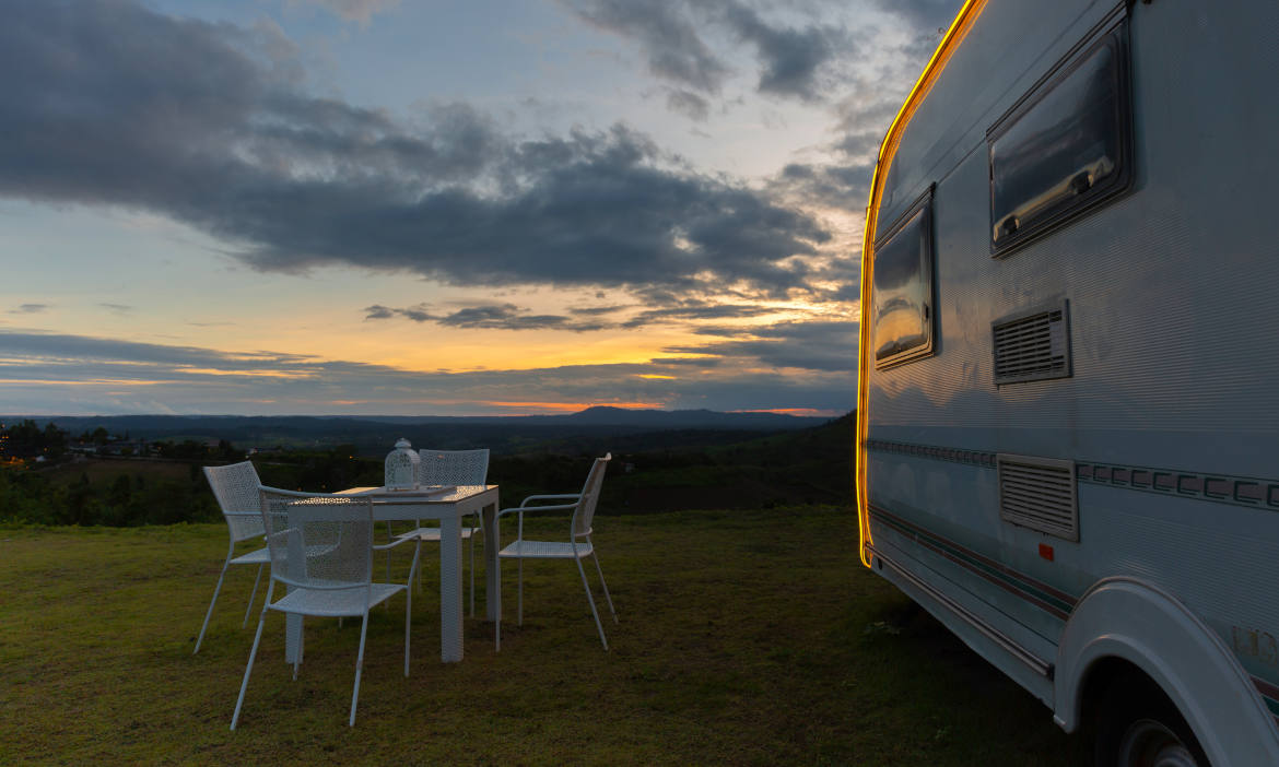 Wohnwagen im Freien bei Sonnenuntergang mit Tisch und Stühlen.