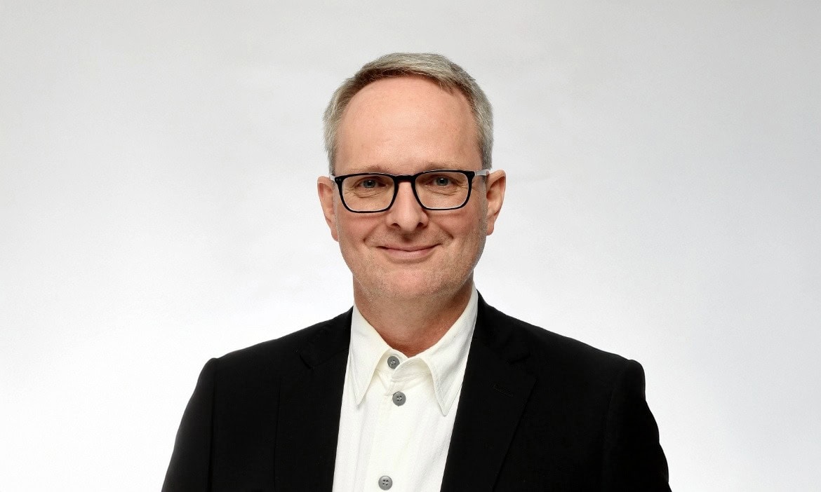 Mann in Anzug und Brille spricht über Riester-Verträge und Altersvorsorge.