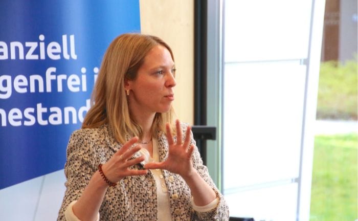 Frau erklärt Finanzthemen bei Beratungsgespräch, sitzt vor Fenster.