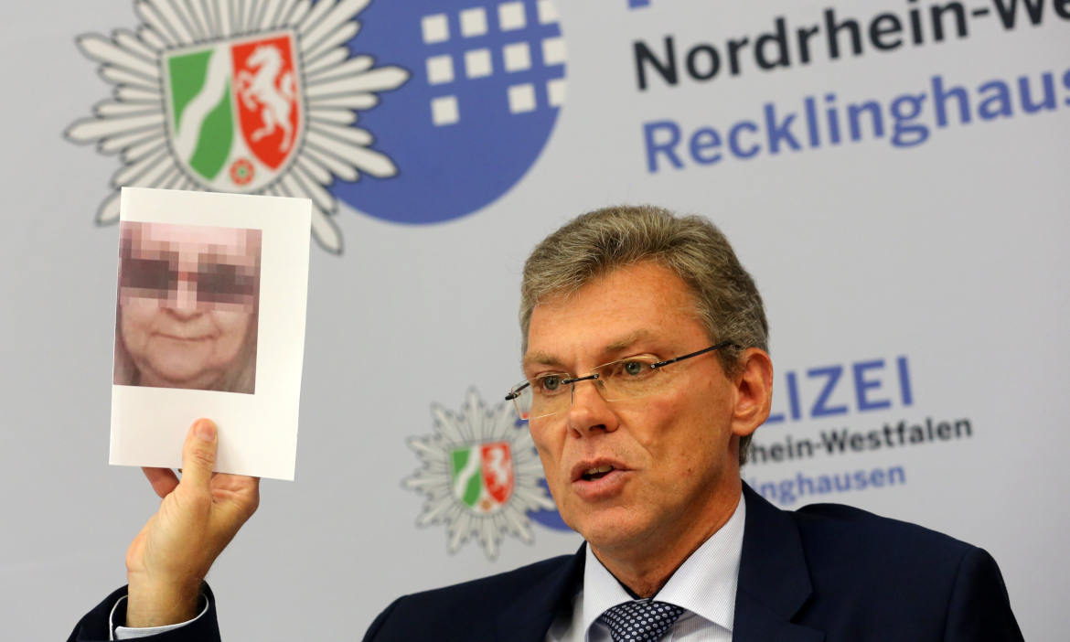 Mann bei Pressekonferenz erklärt Lösegeldversicherung, im Hintergrund Polizei- und Landeswappen.