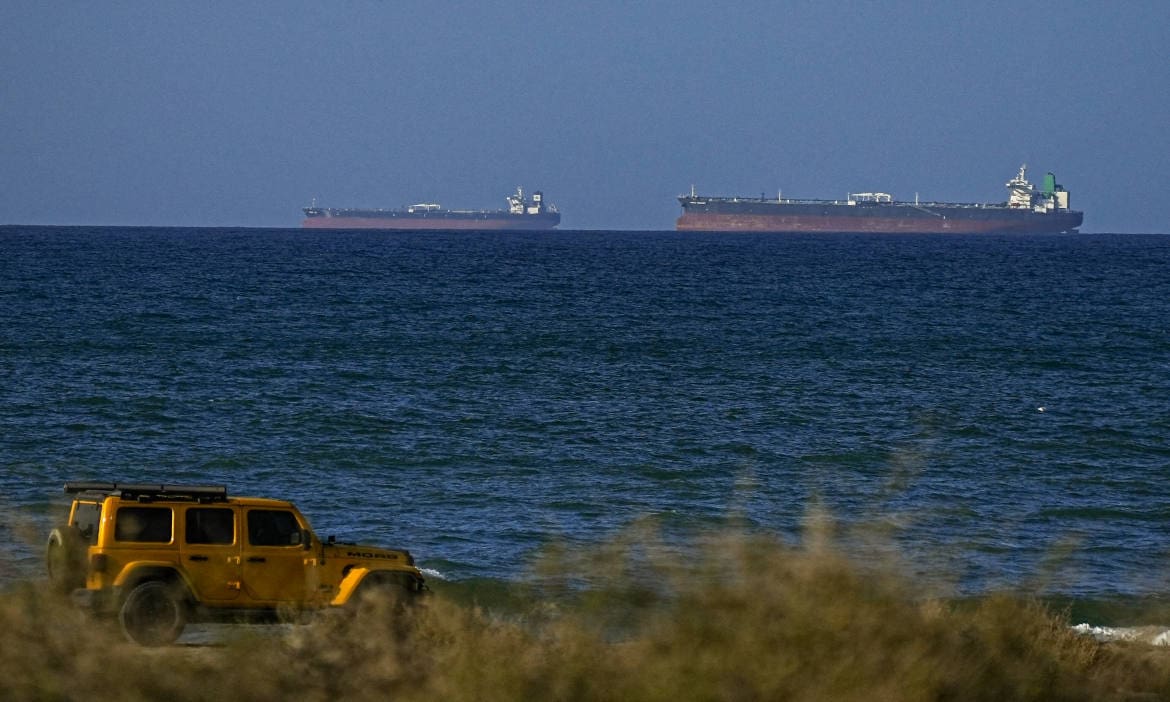 Großes Frachtschiff auf offener See mit Geländewagen am Strand im Vordergrund.