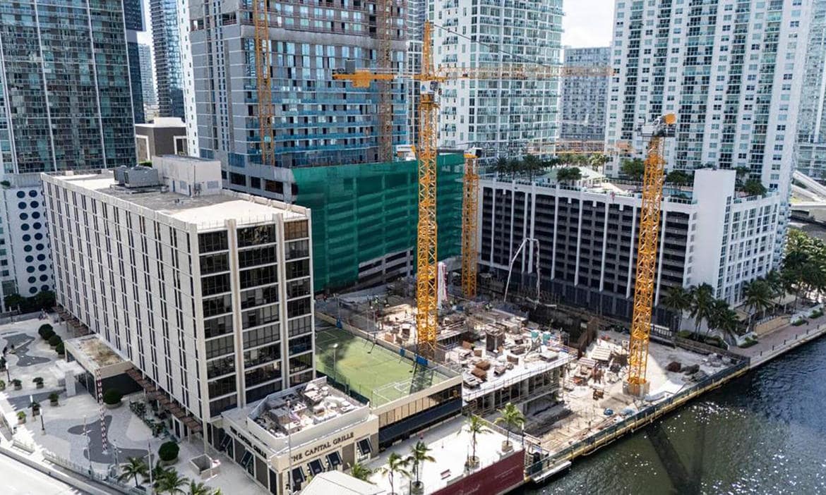 Hochhaus-Bau in Miami mit Kräne und Wasser im Vordergrund.