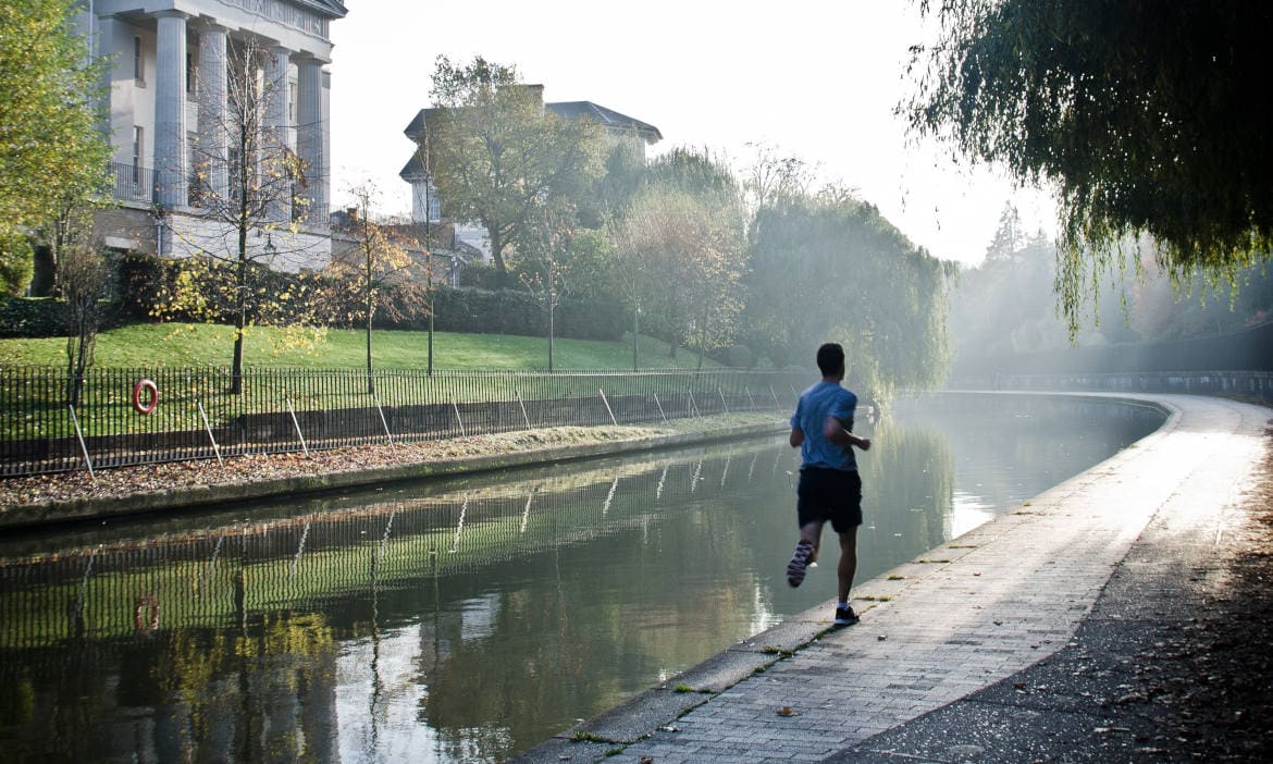 Jogger läuft am Fluss entlang bei ruhiger Morgenstimmung.