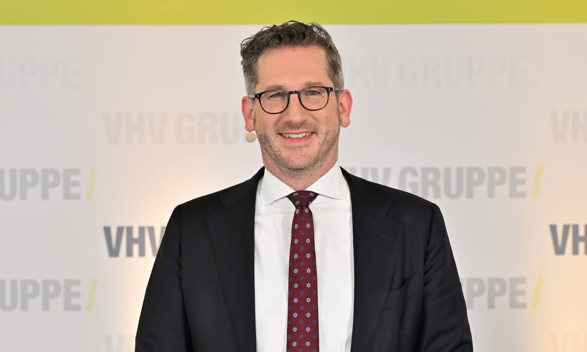 Mann in Anzug bei VHV KFZ-Versicherung mit freundlichem Lächeln.