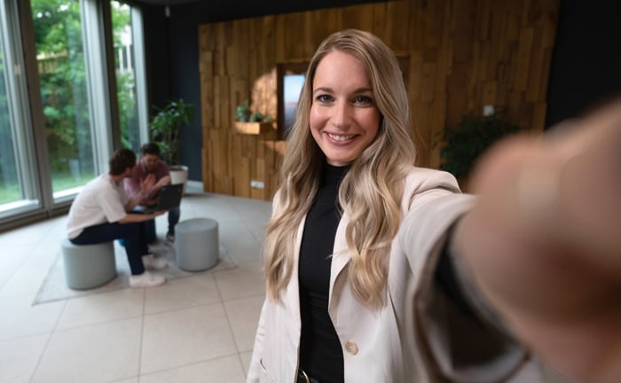Selbstbewusste Frau nimmt ein Selfie im modernen Büro mit großen Fenstern und natürlichem Licht.