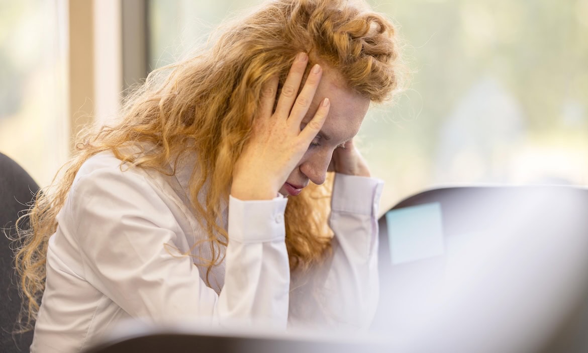 Frau mit Kopfschmerzen am Arbeitsplatz, berufsunfähig in Deutschland.