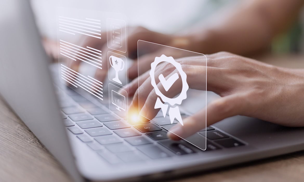 Person tippt auf Laptop mit digitalem Gütesiegel und Leistungsicons.