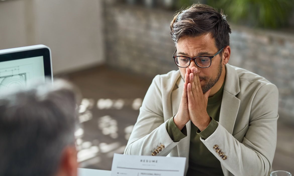 Mann mit besorgtem Gesicht hält Hände vor Mund, symbolisiert Stress bei Konflikten.