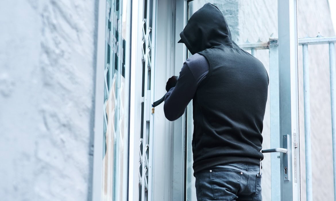 Ein Einbrecher versucht, eine Tür mit einem Werkzeug aufzubrechen.