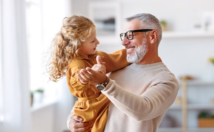 Vater und Tochter lachen fröhlich im Wohnzimmer, teilen einen besonderen Moment.