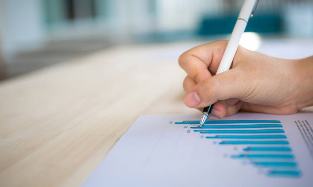 Hand mit Kugelschreiber analysiert Finanzdiagramm zur Lebensversicherung 2025.