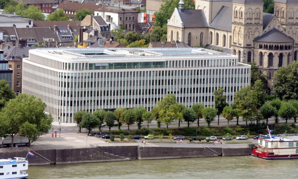 Zeitgenössisches Bürogebäude am Fluss mit großen Fenstern und umgeben von Bäumen.