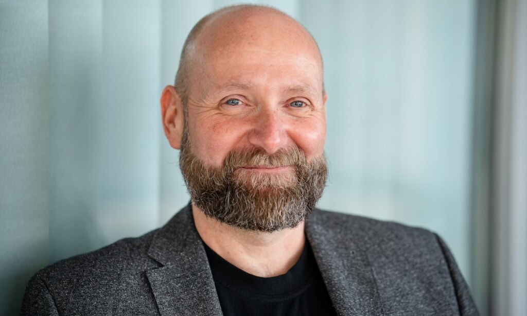 Mann mit Bart in Businesskleidung vor Fenster, professionelles Porträt.