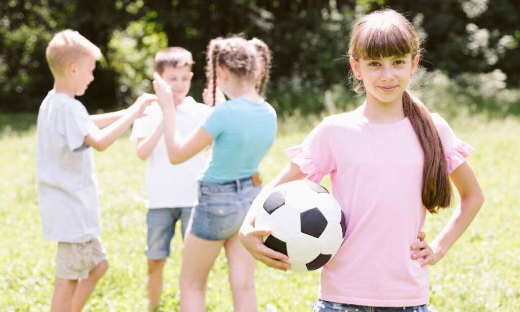 Fröhliches Mädchen mit Fußball im Park, Kinder spielen im Freien, Spaß und Bewegung.