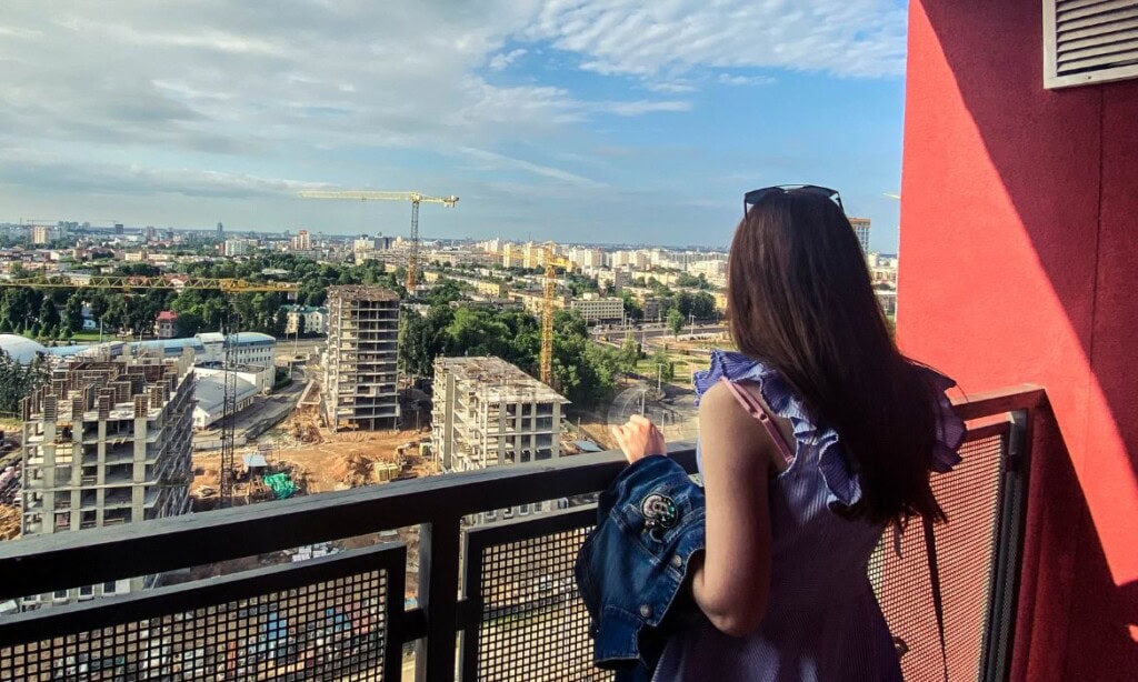 Frau schaut auf die Stadt vom Balkon mit Bauprojekten und Skyline im Hintergrund.