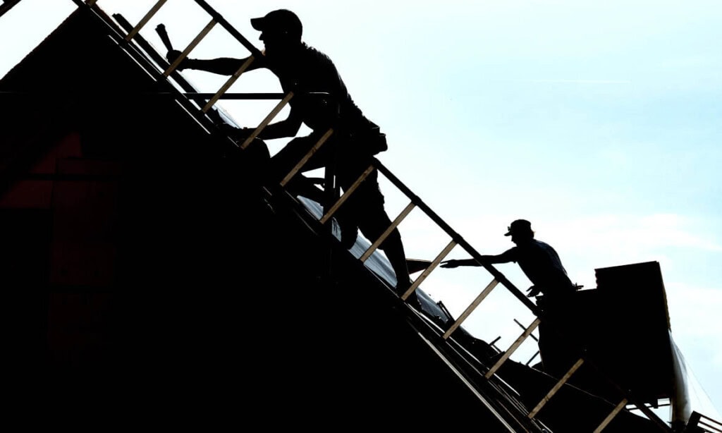 Dachdecker bei der Arbeit auf einem Dach, Silhouette gegen den Himmel.