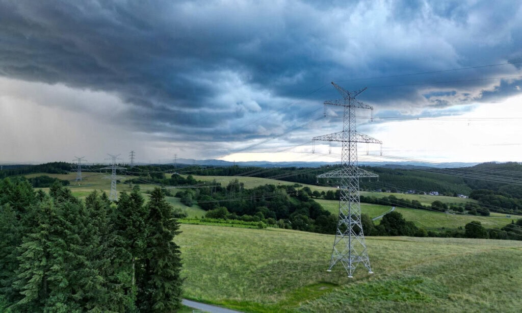 Hochspannungsleitungen in einer ländlichen Landschaft bei dunklem Himmel.